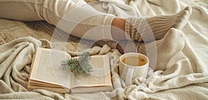 Cozy winter evening , warm woolen socks. Woman is lying feet up on white shaggy blanket and reading book. Cozy leisure scene