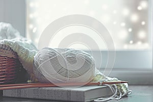 Cozy winter home with warm knitted sweaters and ball of yarn near windowsill, home hobbies