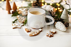 Cozy winter mood. Coffee with gingerbread cookies, pine cones and warm lights on white wooden table