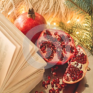 Cozy winter morning at home. Book and Pomegranate in a winter composition, Christmas trees, cones. Warm pillows and garlands