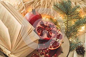 Cozy winter morning at home. Book and Pomegranate in a winter composition, Christmas trees, cones. Warm pillows and garlands