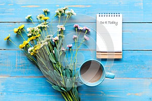 Cozy winter relax time.  Cup of hot coffee with write note on paper and flower on the blue wood background