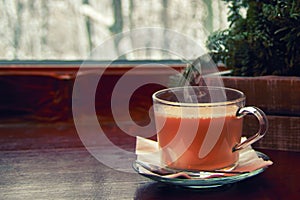 Cozy winter still life: glass cup hot cocoa with steam, on wooden windowsill against snow landscape from outside.