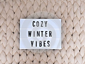 COZY WINTER VIBES word on lightbox on knit background. Cozy compozition. Knit background.