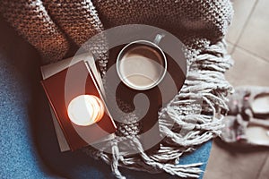 Cozy winter weekend at home. Morning with coffee or cocoa, books, warm knitted blanket and nordic style chair. Hygge concept.