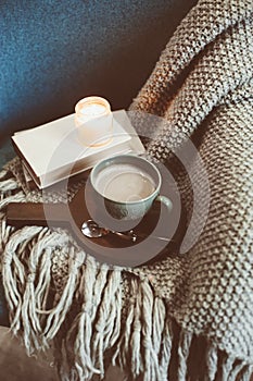 Cozy winter weekend at home. Morning with coffee or cocoa, books, warm knitted blanket and nordic style chair. Hygge concept.