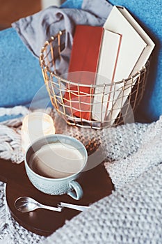 Cozy winter weekend at home. Morning with coffee or cocoa, books, warm knitted blanket and nordic style chair. Hygge concept.