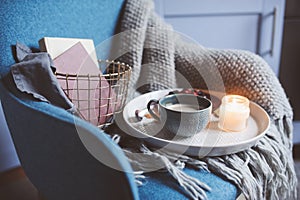 Cozy winter weekend at home. Morning with coffee or cocoa, books, warm knitted blanket and nordic style chair. Hygge concept.