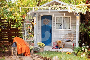 Cozy wooden house porch with chair, blanket, potted chrysanthemums and pumpkins. Decor outdoor of autumn yard. Facade House decora