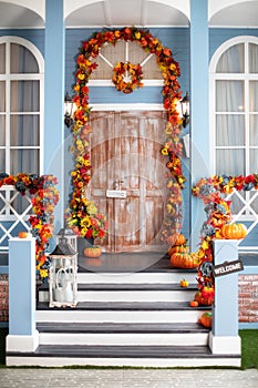 Cozy wooden porch of the house with pumpkins in fall time. House entrance staircase decorated for autumn holidays, fall flowers an