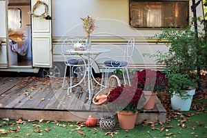 Cozy wooden RV house porch with garden furniture. Decor summer yard. Interior cozy patio with chrysanthemums in pots. Table and ch