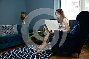 Cozy young asian woman freelancer sit on modern sofar and open or close the laptop with green palm tree in living room at home