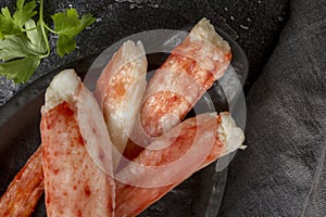 Crab sticks on black plate with parsley at black background