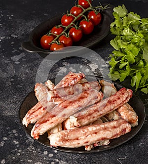 Crab sticks on black plate with parsley and tomatoes at black background