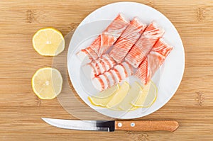 Crab sticks, knife and pieces of lemon in white plate