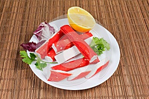 Crab sticks, lemon and greens on dish on table mat