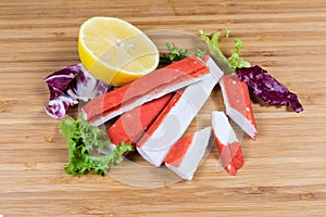 Crab sticks, lemon and variegated lettuce leaves on cutting board