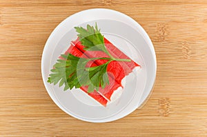 Crab sticks with parsley in white saucer on table