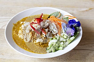 Crabmeat curry sauce with fermented rice noodle and side dishes in white plate on the wooden table.