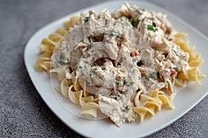 Crack chicken slow cooked dish over egg pasta on a white plate