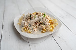 Crack chicken slow cooked dish over egg pasta on a white plate