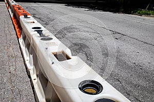 Cracked asphalt city street divided with white and orange hard plastic traffic barricades, urban decay and street restoration