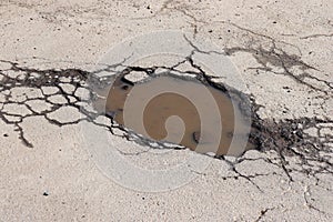 Cracked asphalt road with water puddle. Old pavement textured background with cracks.