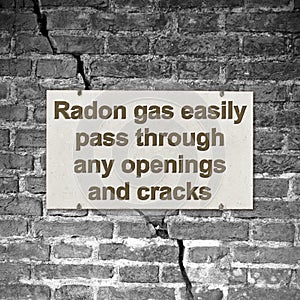 A cracked brick wall with warning message abaut radon gas escaping through cracks and openings - concept image photo