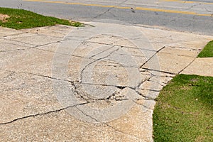 Cracked and broken aggregate concrete driveway descending into an asphalt roadway, flanked by green grassy areas, creative copy sp