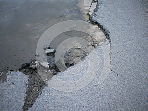 Cracked and broken asphalt pothole with water on the surface of