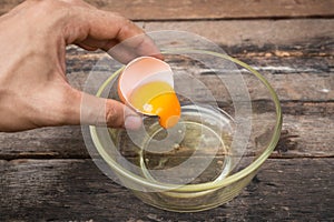 Cracked chicken egg with yolk and egg shell on dish, wooden background