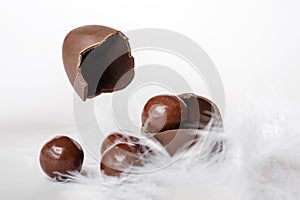 Cracked chocolate easter egg with chocolate small round candies and flying eggshell in white feather nest