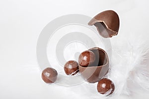 Cracked chocolate easter egg with chocolate small round candies and flying eggshell in white feather nest, levitation