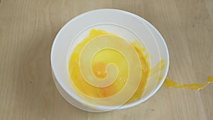Cracked egg falls into white bowl, preparing food on wooden table.