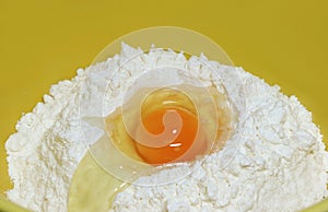 Cracked egg on raw flour in a yellow mixing bowl