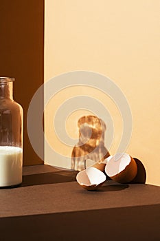 Cracked empty egg shell on brown and beige egg shell with a bottle of milk on brown and beige background