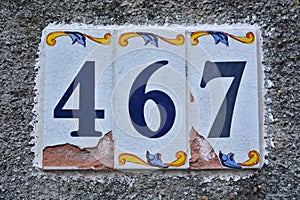 A cracked house number plaque, showing the number four hundred sixty seven 467