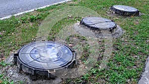 Cracked metallic well cover on Moscow street with small pond reflecting clouded sky