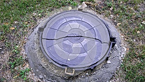 Cracked metallic well cover on Moscow street with small pond reflecting clouded sky