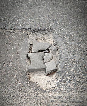 Cracked road, street with pothole, top view. Large pit with stones on the asphalt road, gray color