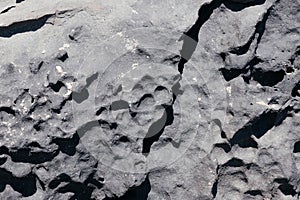 Cracked rough dark grey rock stone texture surface background.