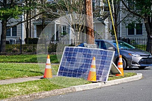 Cracked solar panel on the ground near a utility pole that they fell from with orange warning cones nearby