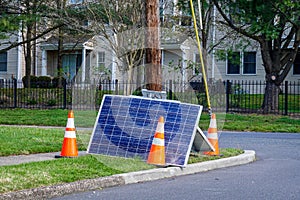 Cracked solar panel on the ground near a utility pole that they fell from with orange warning cones nearby