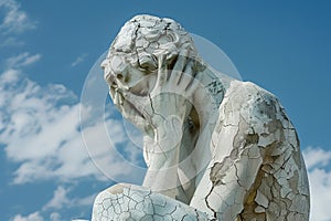Cracked statue of person holding hands to face, symbolizing despair and anguish, A cracked and crumbling statue symbolizing a photo