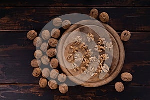 Cracked and whole walnuts on round wooden plate and wooden table, top view. Healthy nuts and seeds composition.