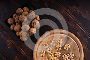 Cracked and whole walnuts on round wooden plate and wooden table, top view. Healthy nuts and seeds composition.