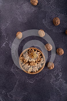 Cracked and whole walnuts in wooden bowl and on dark slate surface. Healthy nuts and seeds composition.