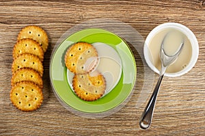 Crackers, cookies in saucer with condensed milk, bowl with milk and spoon on table. Top view
