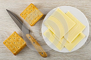 Crackers, kitchen knife, plate with slices of cheese on table. Top view
