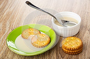 Crackers in saucer with condensed milk, spoon in bowl with milk, cookies on table